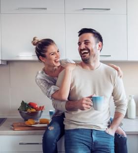 Happy couple smiling, woman sitting on counter with her arm around guy